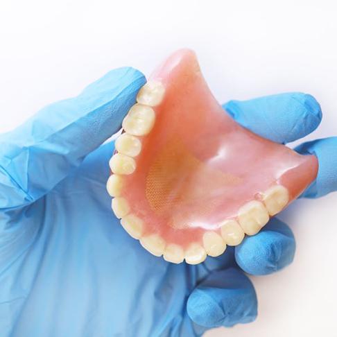 Gloved hand holding denture against white background