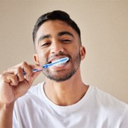 Man in white shirt smiling while brushing his teeth