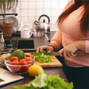 Woman chopping vegetables while following recipe on laptop