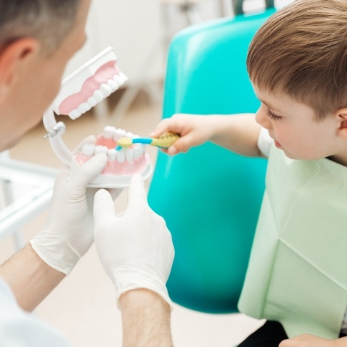 Dentist teaching child to brush teeth during children's dentistry visit
