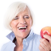 woman about to eat an apple with permanent implant dentures in Brookfield