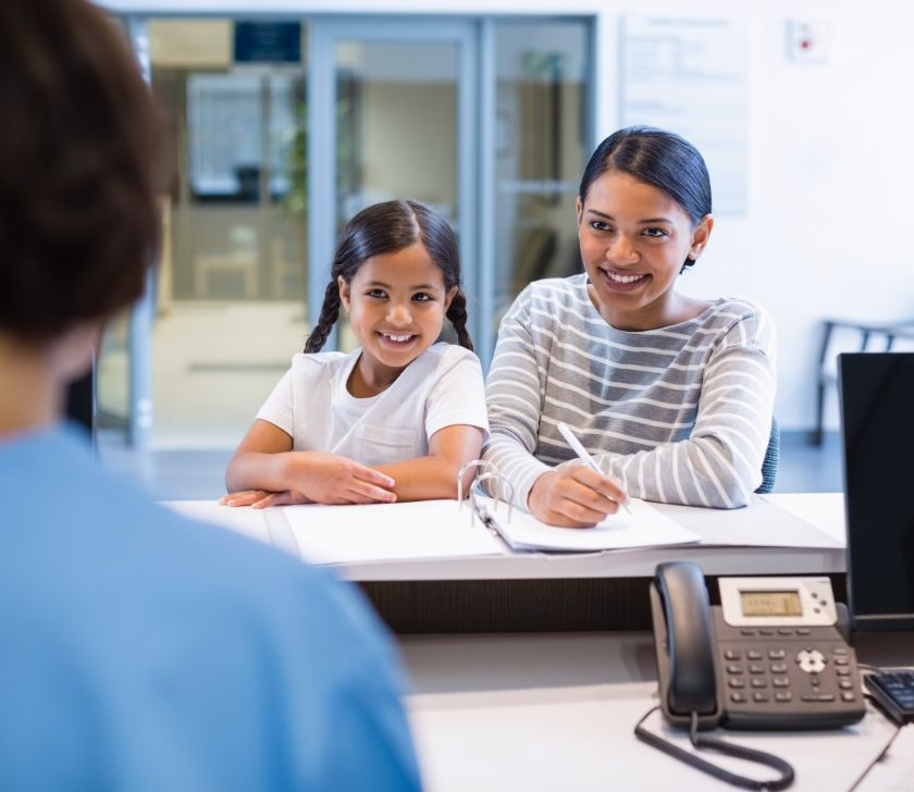 Mother and child at dental office reception desk filling out dental insurance forms