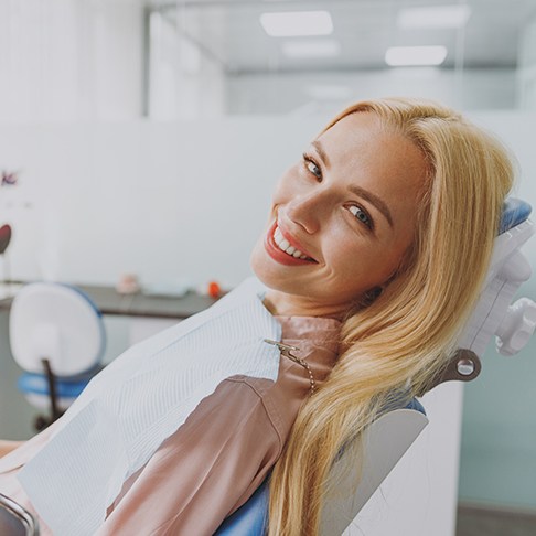 Blonde woman sitting back in dental chair and smiling