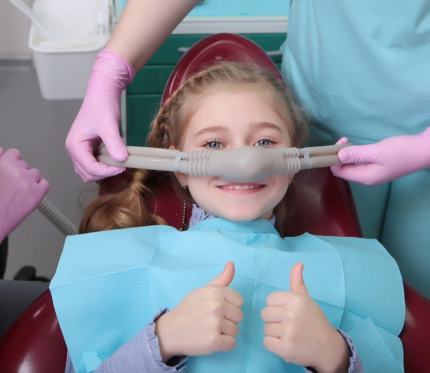 Dentist placing nitrous oxide sedation dentistry mask on young dental patient